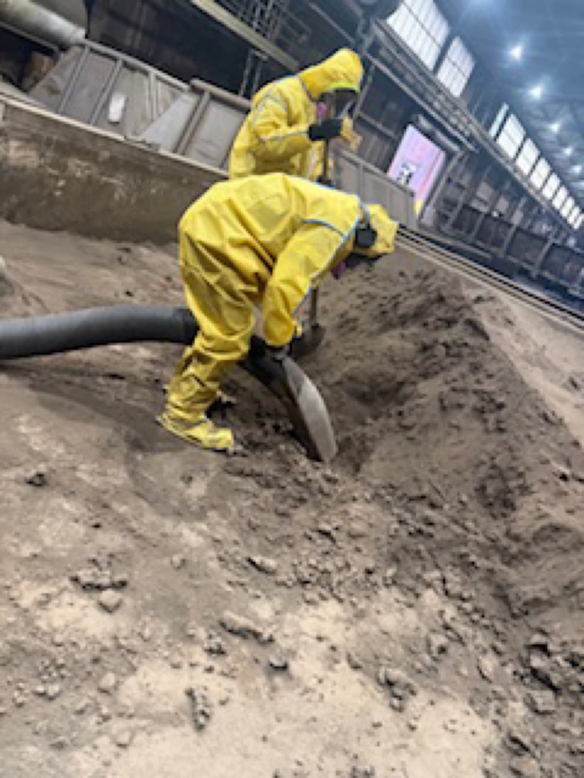 Worker in yellow hazmat suit vacuuming inside industrial facility